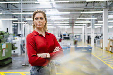 Contemplative businesswoman standing with arms crossed at factory - DIGF19458