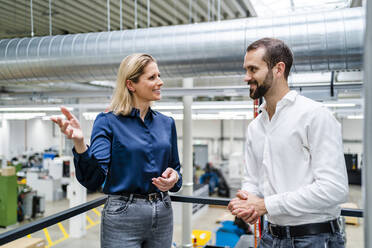 Smiling businesswoman gesturing and talking to colleague near railing at factory - DIGF19462