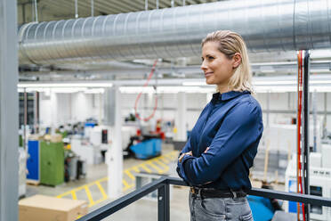 Smiling businesswoman standing with arms crossed near railing in factory - DIGF19464