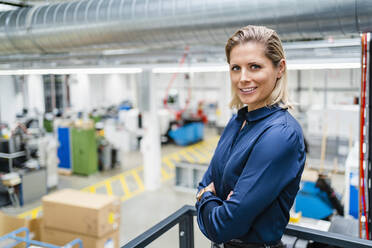 Confident businesswoman wearing blue shirt standing with arms crossed at factory - DIGF19465