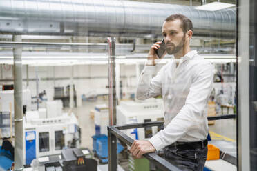 Junger Geschäftsmann spricht mit seinem Smartphone und hält ein Geländer in einer Fabrik - DIGF19468