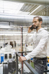 Young businessman talking on smart phone in industry seen through glass - DIGF19469