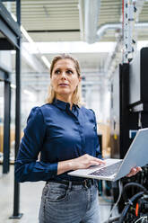 Thoughtful businesswoman with laptop standing in industry - DIGF19481