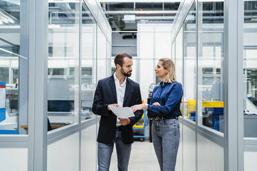 Businesswoman discussing with colleague holding documents at factory - DIGF19508