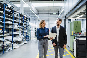 Businesswoman discussing with colleague over tablet PC walking in warehouse at factory - DIGF19523