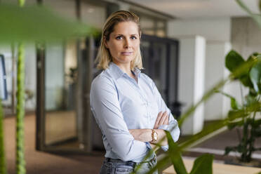 Confident businesswoman with arms crossed at workplace - DIGF19525