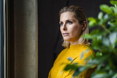 Contemplative businesswoman wearing yellow sweater at workplace - DIGF19552