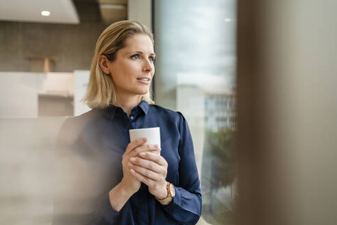 Nachdenkliche Geschäftsfrau mit Kaffeetasse im Büro - DIGF19579