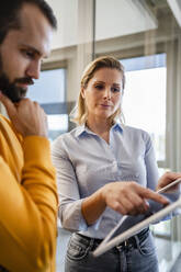 Businesswoman explaining colleague through tablet PC at office - DIGF19604