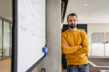 Confident businessman with arms crossed leaning on wall at office - DIGF19635