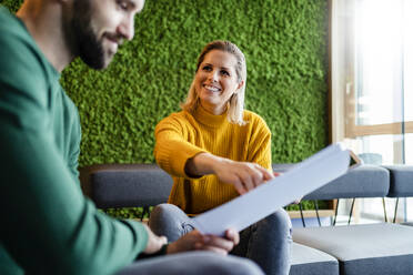 Happy businesswoman explaining document to businessman at office - DIGF19645