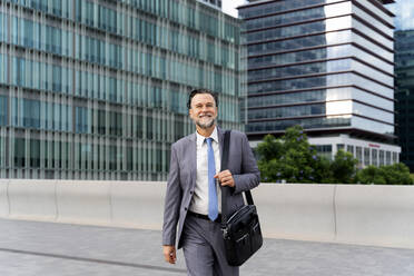 Smiling mature businessman walking on footpath - OIPF02697