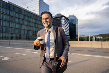 Lächelnder reifer Geschäftsmann mit Einweg-Kaffeebecher auf der Straße - OIPF02698