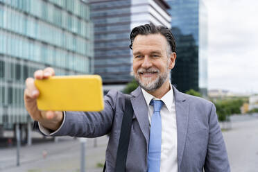 Happy mature businessman taking selfie through smart phone outside building - OIPF02703