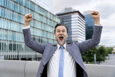 Cheerful businessman showing fists outside building - OIPF02706