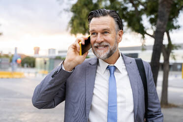 Smiling mature businessman talking on smart phone at street - OIPF02716