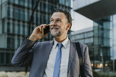 Contemplative mature businessman talking on smart phone in front of building - OIPF02725