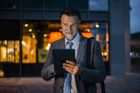 Lächelnder reifer Geschäftsmann mit Tablet-PC auf dem Fußweg stehend - OIPF02729