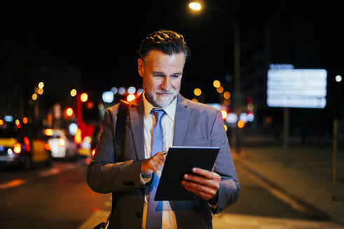 Lächelnder reifer Geschäftsmann bei der Verwendung eines Tablet-PCs in der Nacht - OIPF02735