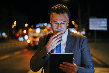 Thoughtful mature businessman standing with tablet PC at street - OIPF02736