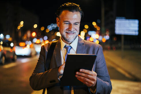 Glücklicher reifer Geschäftsmann bei der Nutzung eines Tablet-PCs in der Nacht - OIPF02738