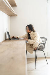 Young freelancer working on laptop at desk in home office - DLTSF03480