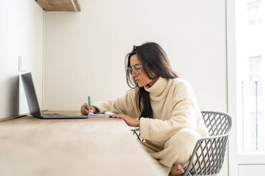 Young woman writing in diary and working at home office - DLTSF03481