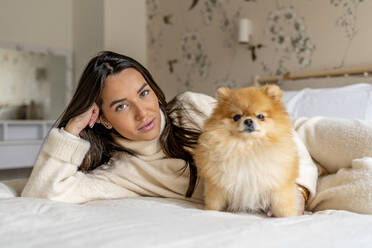 Smiling young woman lying with dog on bed at home - DLTSF03482