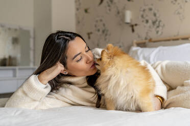 Junge Frau umarmt und küsst Hund auf dem Bett zu Hause - DLTSF03483
