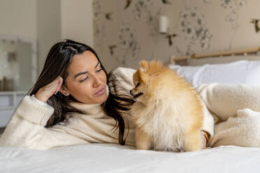 Smiling young woman with cute dog on bed at home - DLTSF03484