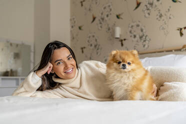 Glückliche junge Frau auf dem Bett liegend mit Hund zu Hause - DLTSF03485