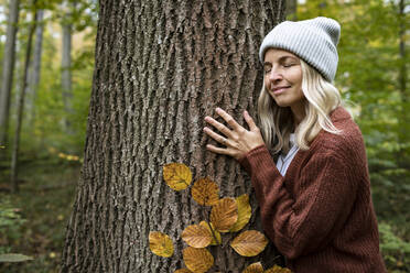 Mature woman hugging tree in autumn forest - HMEF01438