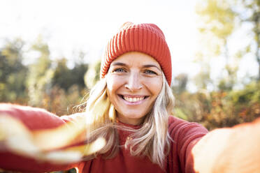 Lächelnde blonde reife Frau, die ein Selfie mit orangefarbener Strickmütze macht - HMEF01458