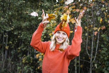 Happy mature woman throwing autumn leaves in forest - HMEF01464