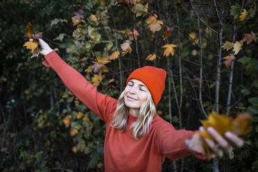 Mature woman holding autumn leaves with eyes closed in forest - HMEF01465