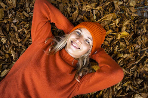 Lächelnde reife Frau liegt mit den Händen hinter dem Kopf auf Herbstblättern - HMEF01473
