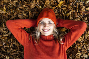 Smiling mature woman with blue eyes lying on autumn leaves - HMEF01474