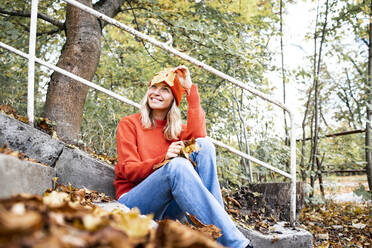 Lächelnde Frau mit Herbstblatt Tagträumen im Park - HMEF01476