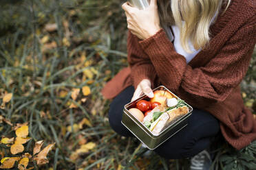 Ältere Frau mit Brotdose im Herbstpark hockend - HMEF01481