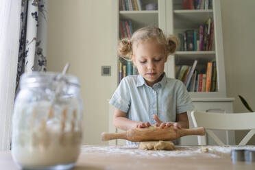Blondes Mädchen rollt Keksteig auf dem Tisch zu Hause - SVKF00778