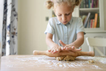 Girl rolling cookie dough on table at home - SVKF00779