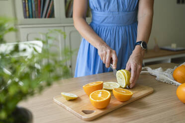 Hände einer Frau, die Zitronen und Orangen auf einem Tisch zu Hause schneidet - SVKF00784