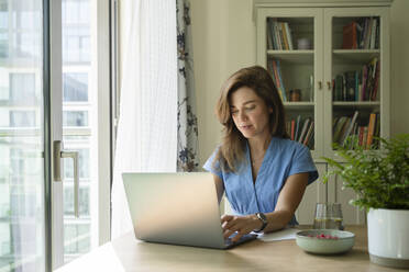 Geschäftsfrau arbeitet an einem Laptop am Schreibtisch im Heimbüro - SVKF00785