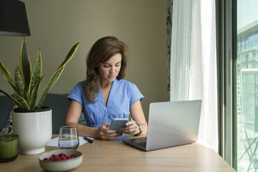 Freelancer using smart phone at desk in home office - SVKF00787
