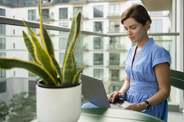 Smiling freelancer using laptop in balcony - SVKF00822