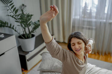 Smiling woman stretching on bed at home - ANAF00536