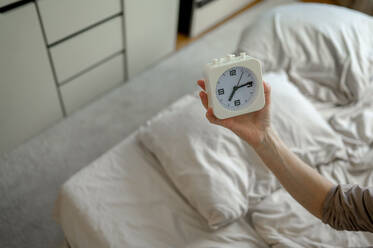 Hand einer Frau hält Wecker im Schlafzimmer - ANAF00539