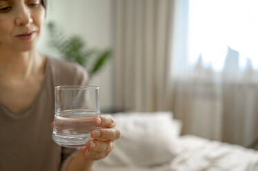 Woman sitting on bed with glass of water at home - ANAF00542