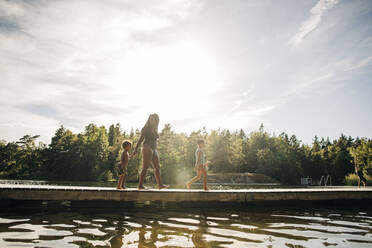 Boy and girl walking with mother on jetty during vacation - MASF32612