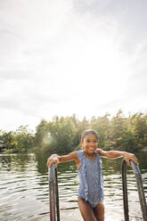 Smiling wet girl holding railing during vacation at lake - MASF32616